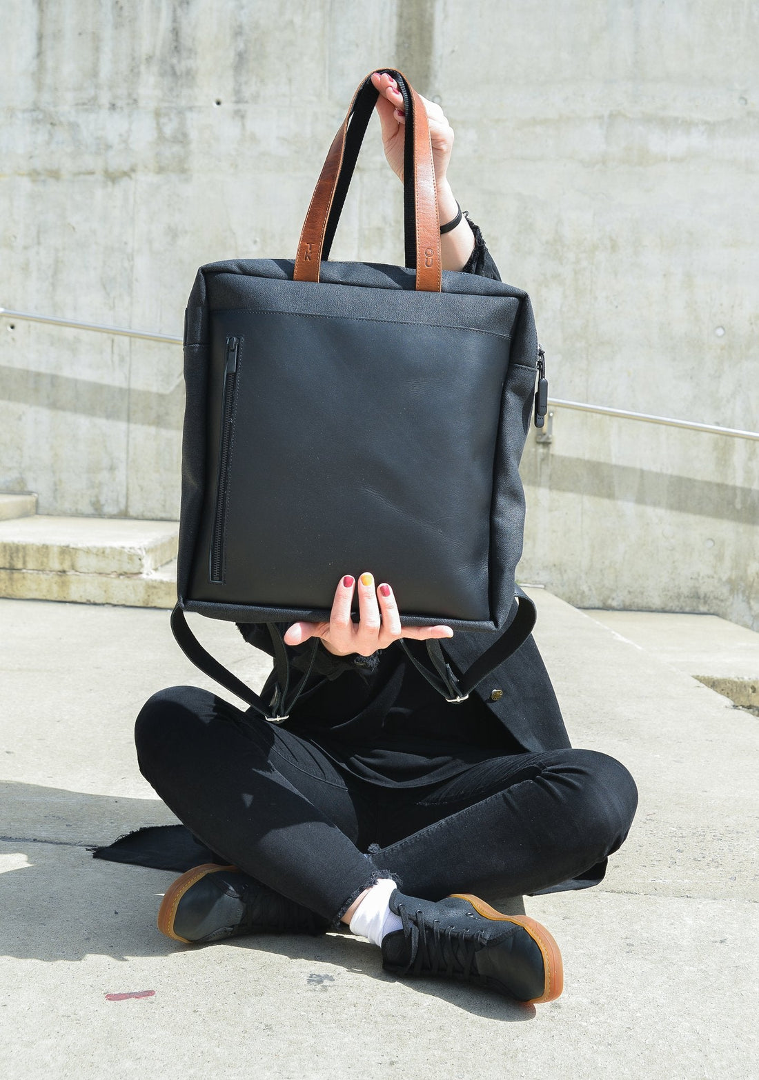 1. Lifestyle image of a person holding the Omaking Stockholm Backpack in black, showcasing its versatile design and front zippered pocket