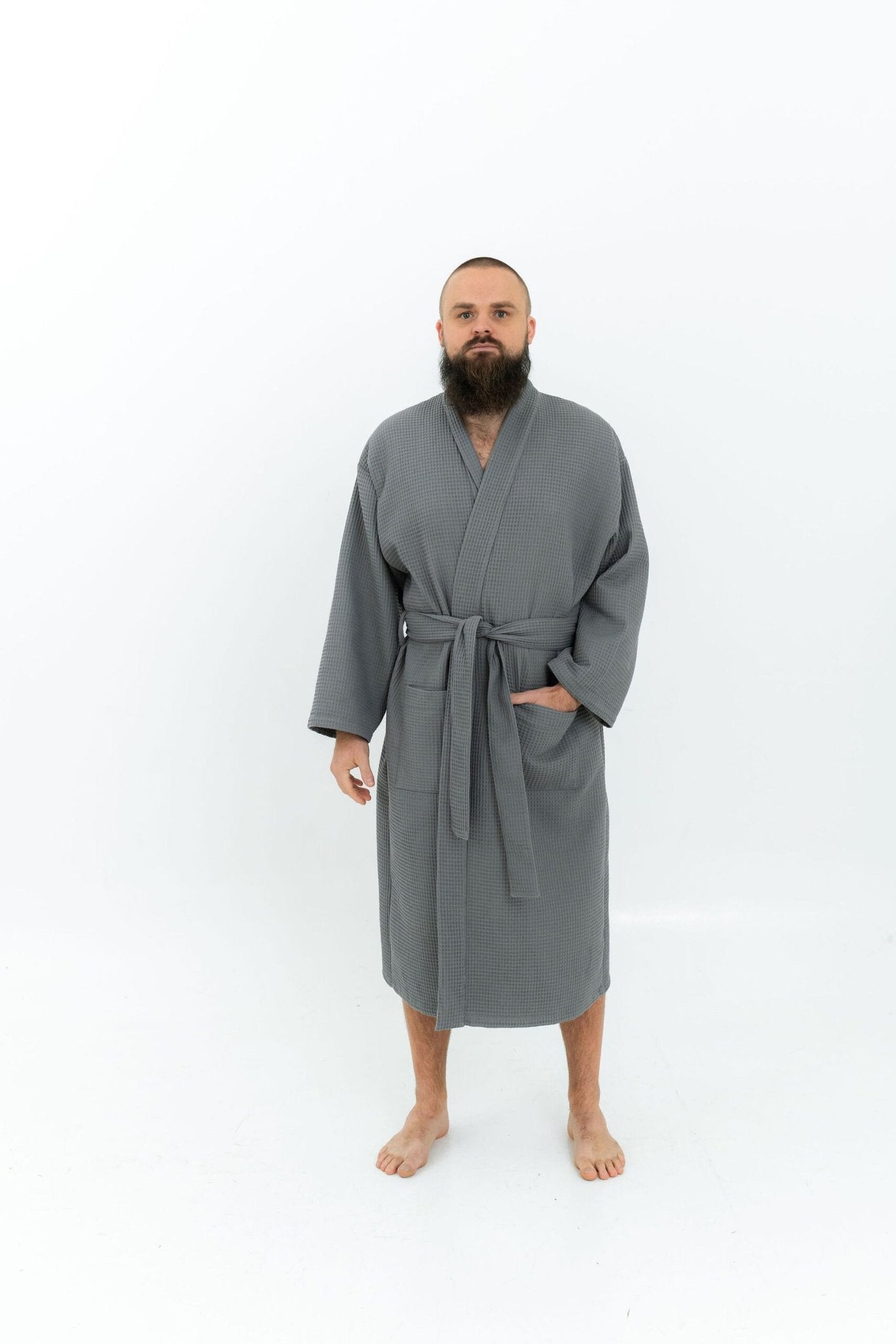 1. Man wearing grey waffle fabric robe with belt and side pockets standing on white background