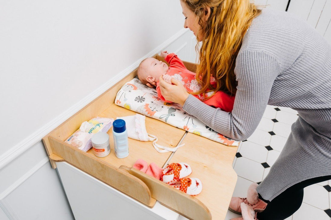 1. Woman changing baby on birch plywood changing table top with diapers and creams nearby in a nursery