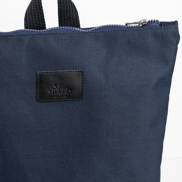 3. Close-up of Muni logo on navy blue waterproof backpack with leather bottom
