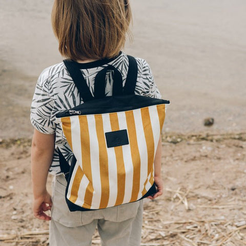 2. Child wearing Muni striped mustard and white backpack on a sandy path
