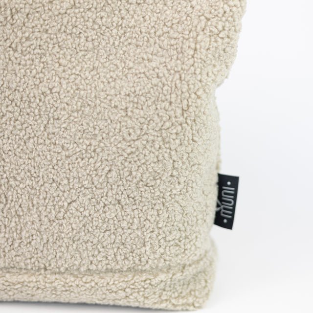 6. Close-up of Muni brand tag on beige teddy backpack, highlighting texture