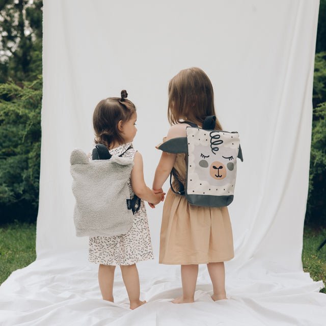 4. Two children wearing Muni sheep backpacks outdoors, showcasing adjustable straps and playful design