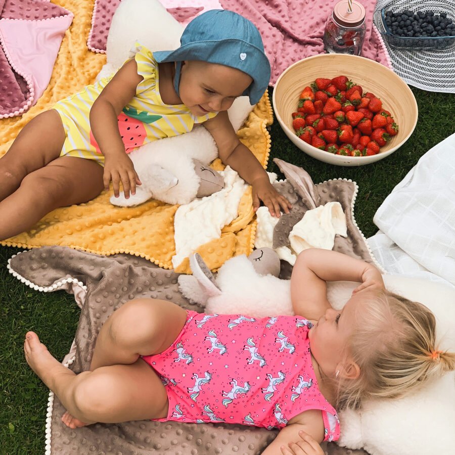 5. Two children relaxing with cream alpaca soft toy-pillows on blankets with strawberries and blueberries nearby