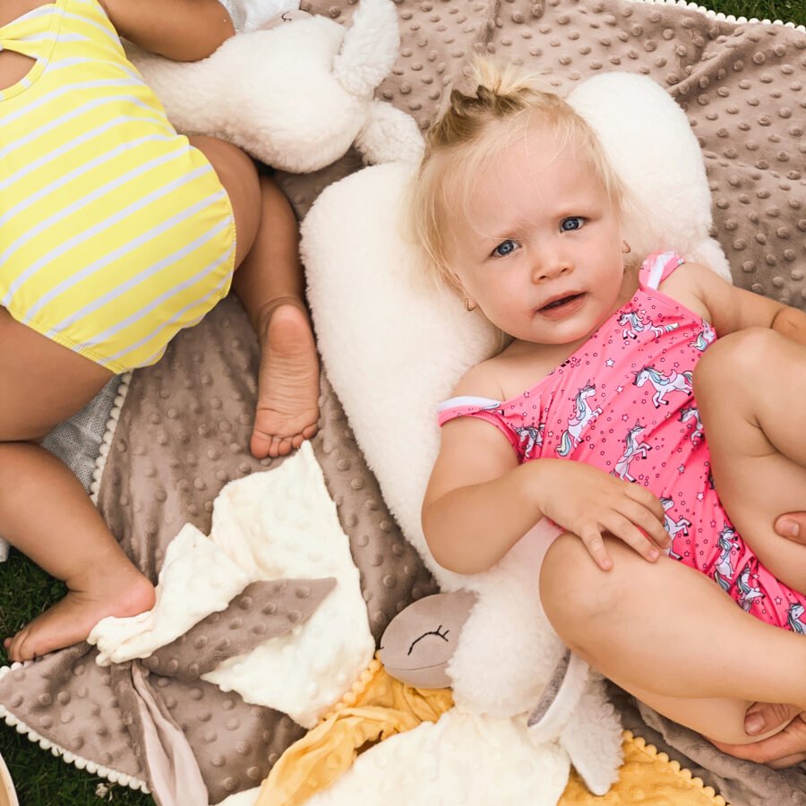 3. Child lying on a cream alpaca soft toy-pillow on a textured blanket outdoors