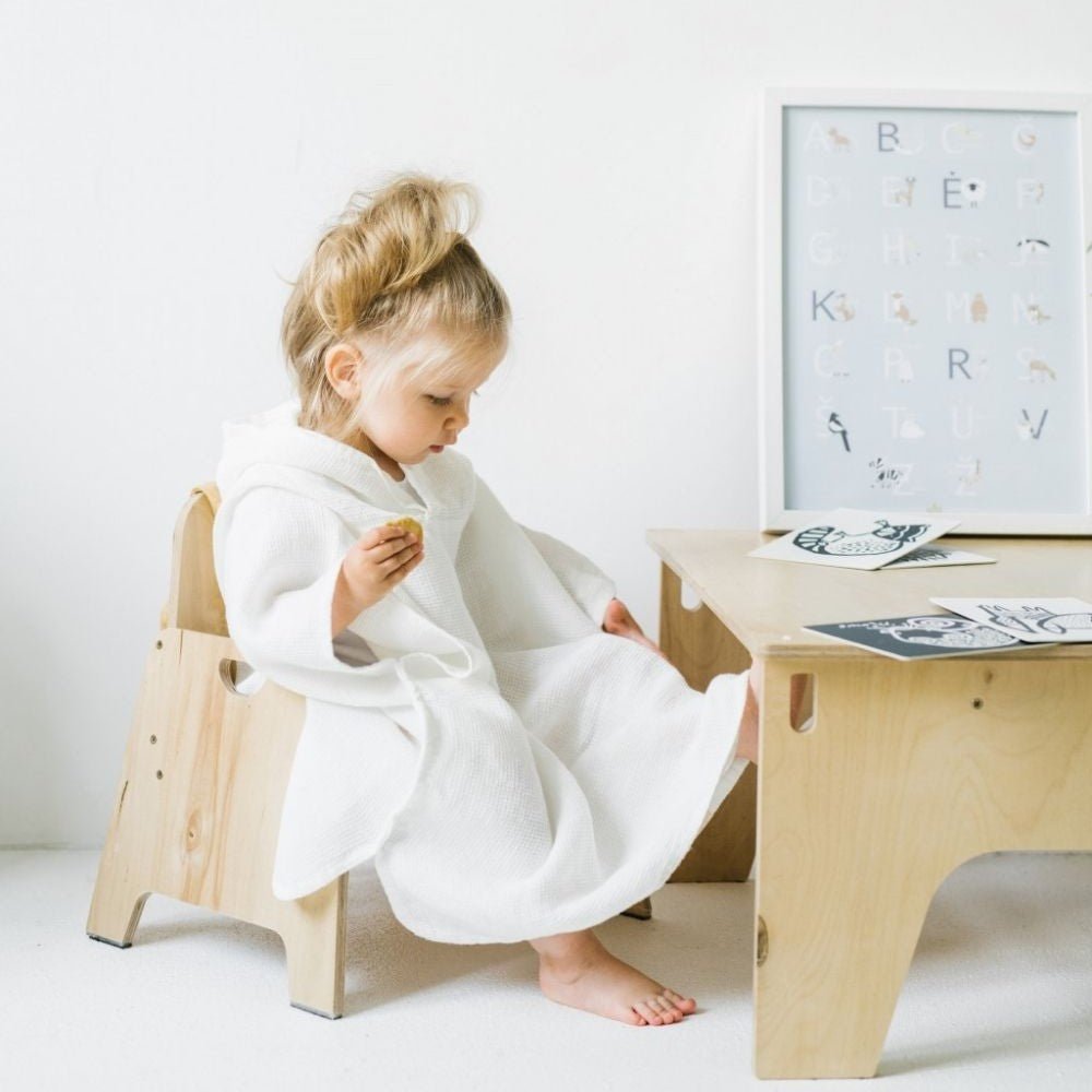 5. Child in white linen waffle poncho seated at a wooden table with educational cards