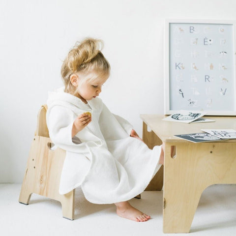 5. Child in white linen waffle poncho seated at a wooden table with educational cards