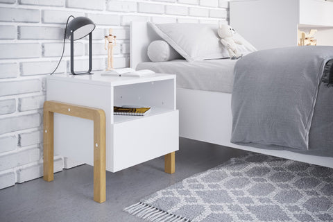 1. Kocot Kids Victor bedside table in children's room setting with white and oak finish, next to bed with grey bedding and decorative items