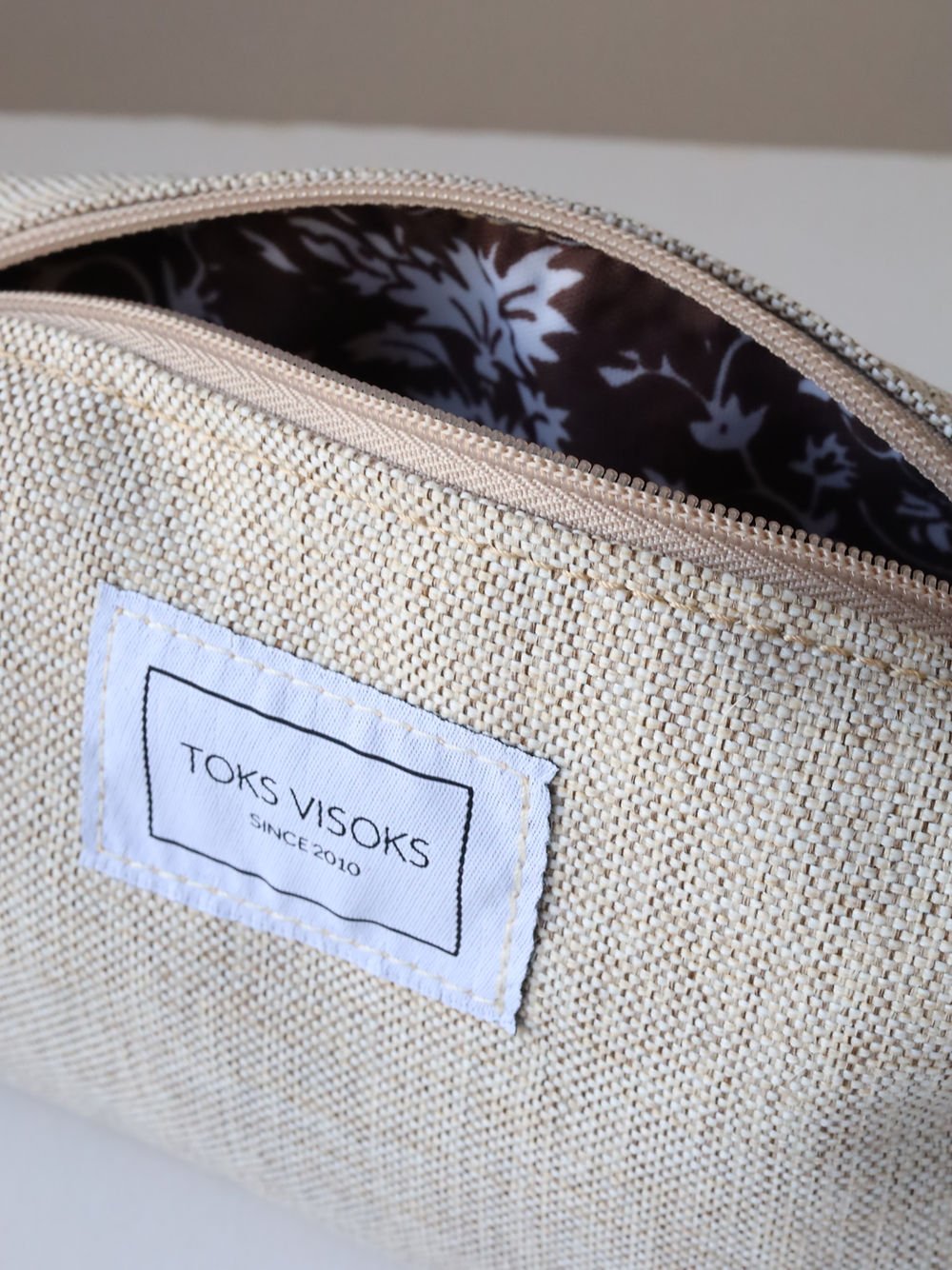 1. Close-up of TOKS VISOKS LORNA Makeup Bag in White Sand, showing interior floral lining and brand label