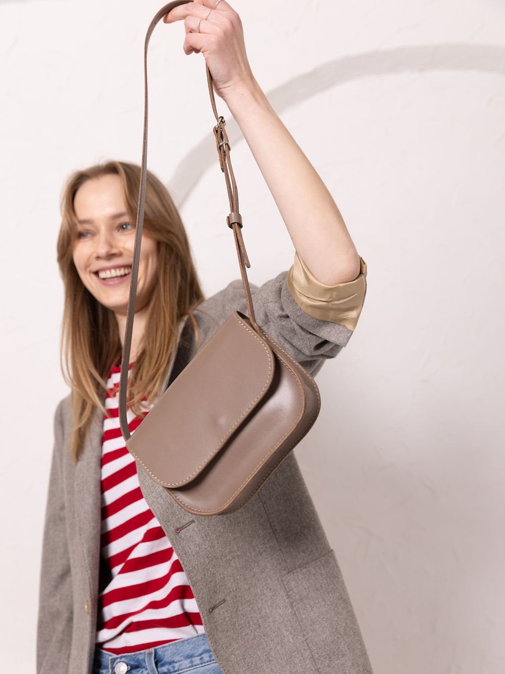 1. Woman holding TOKS VISOKS RUBY Purse in beige with adjustable strap, lifestyle setting
