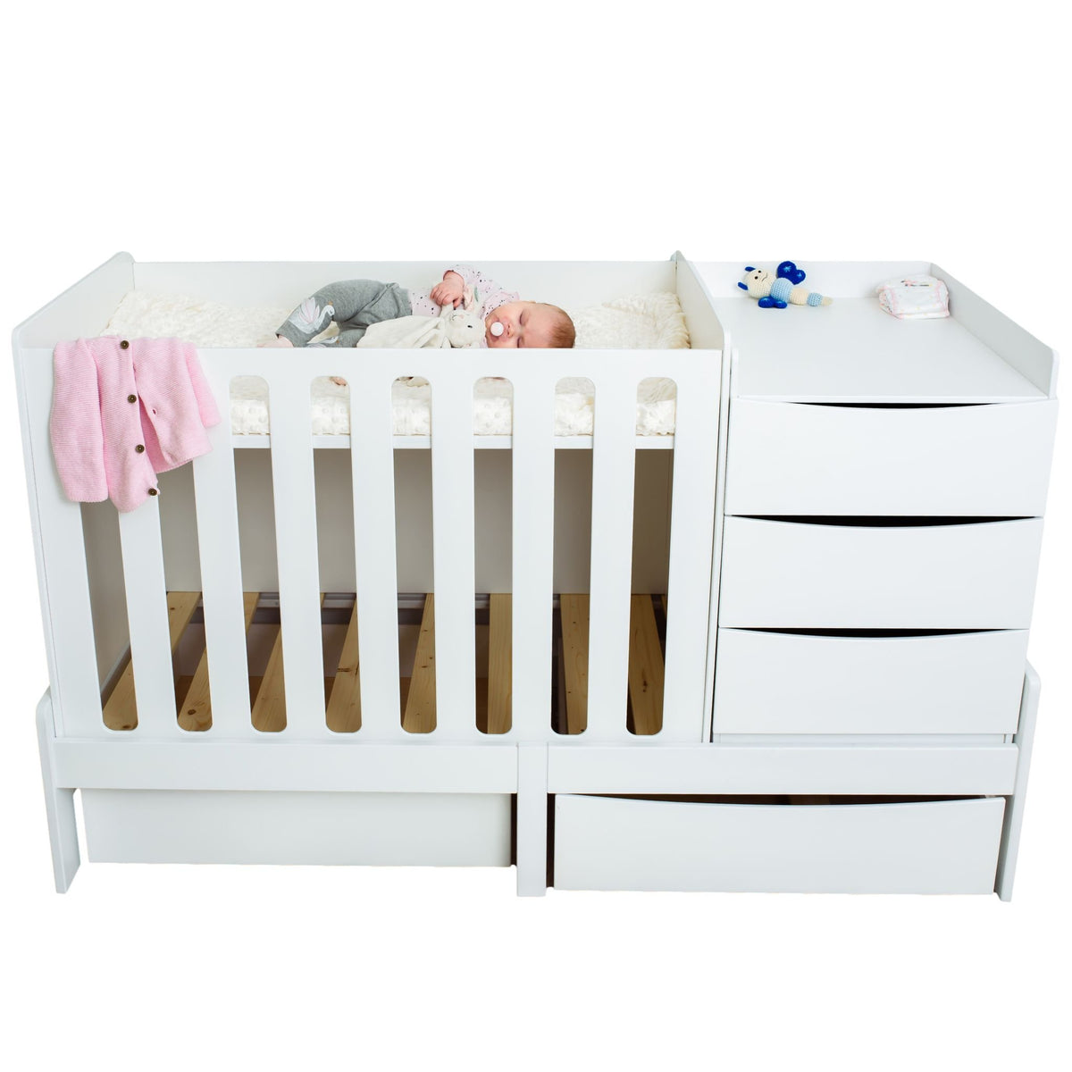 8. Baby sleeping in white crib with attached chest of drawers and pink blanket