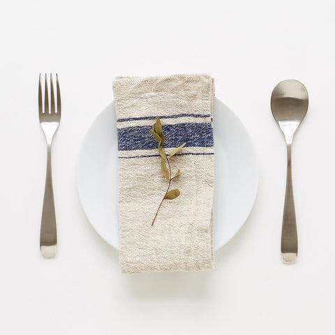 5. Blue striped linen napkin on white plate with dried leaf, set with fork and spoon on white background