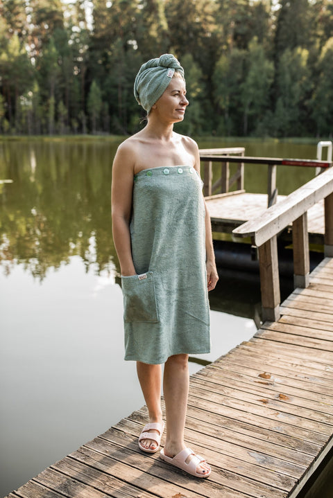 3. Women's light green bamboo terry spa wrap by RÄTT, worn by model on a lakeside dock, featuring button closure and pocket