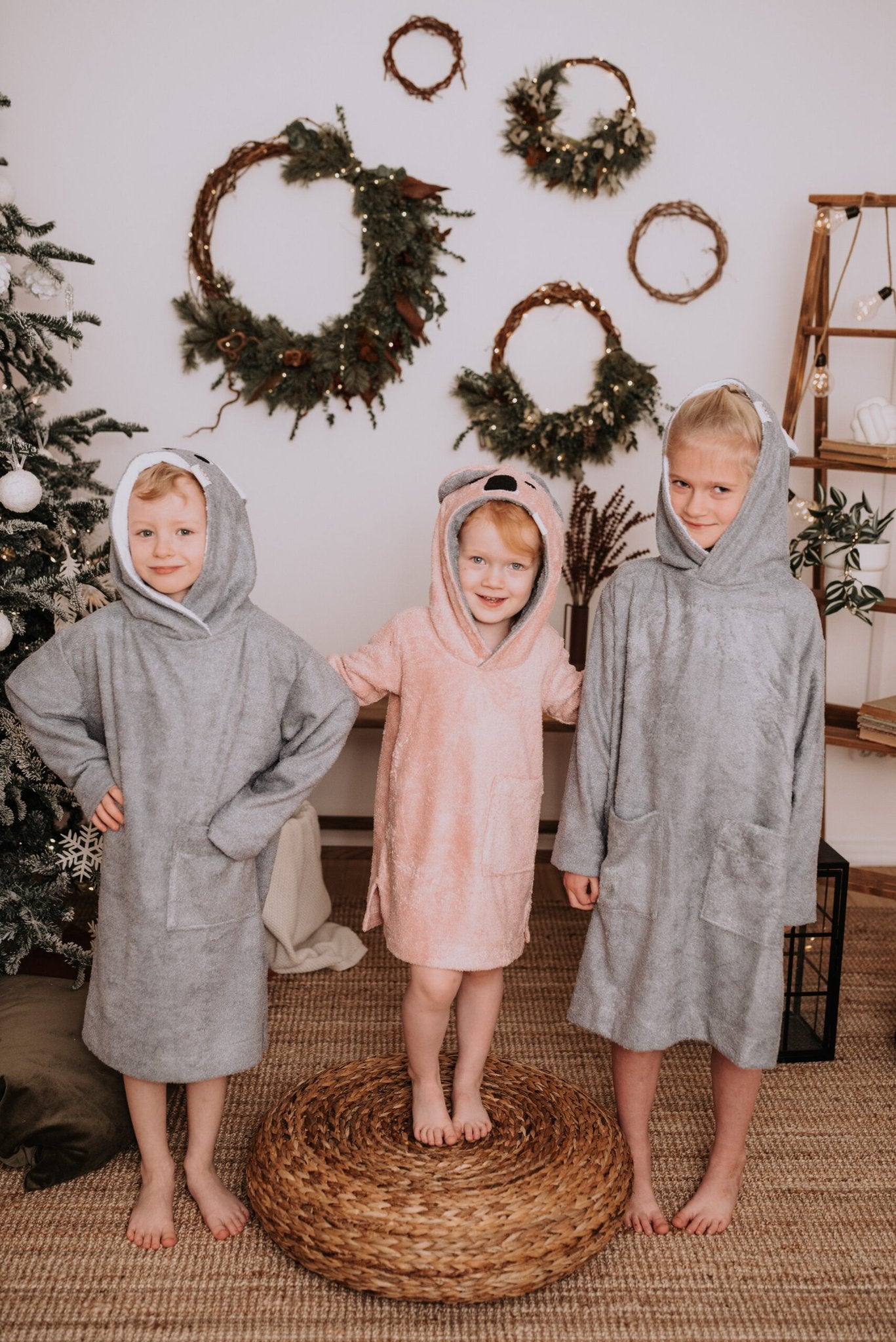 1. Toddlers wearing RÄTT long-sleeve poncho KOALA in pink and grey, shown in a cozy indoor setting