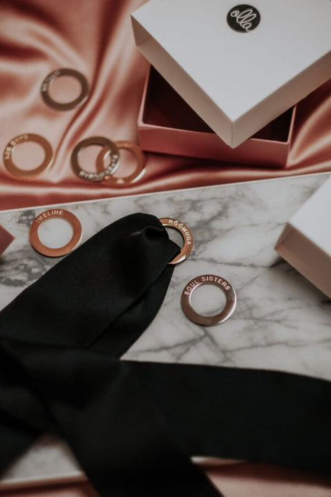 4. Flat lay of black silk ribbon with 'SOUL SISTERS' engraved rings on marble surface, Olla packaging