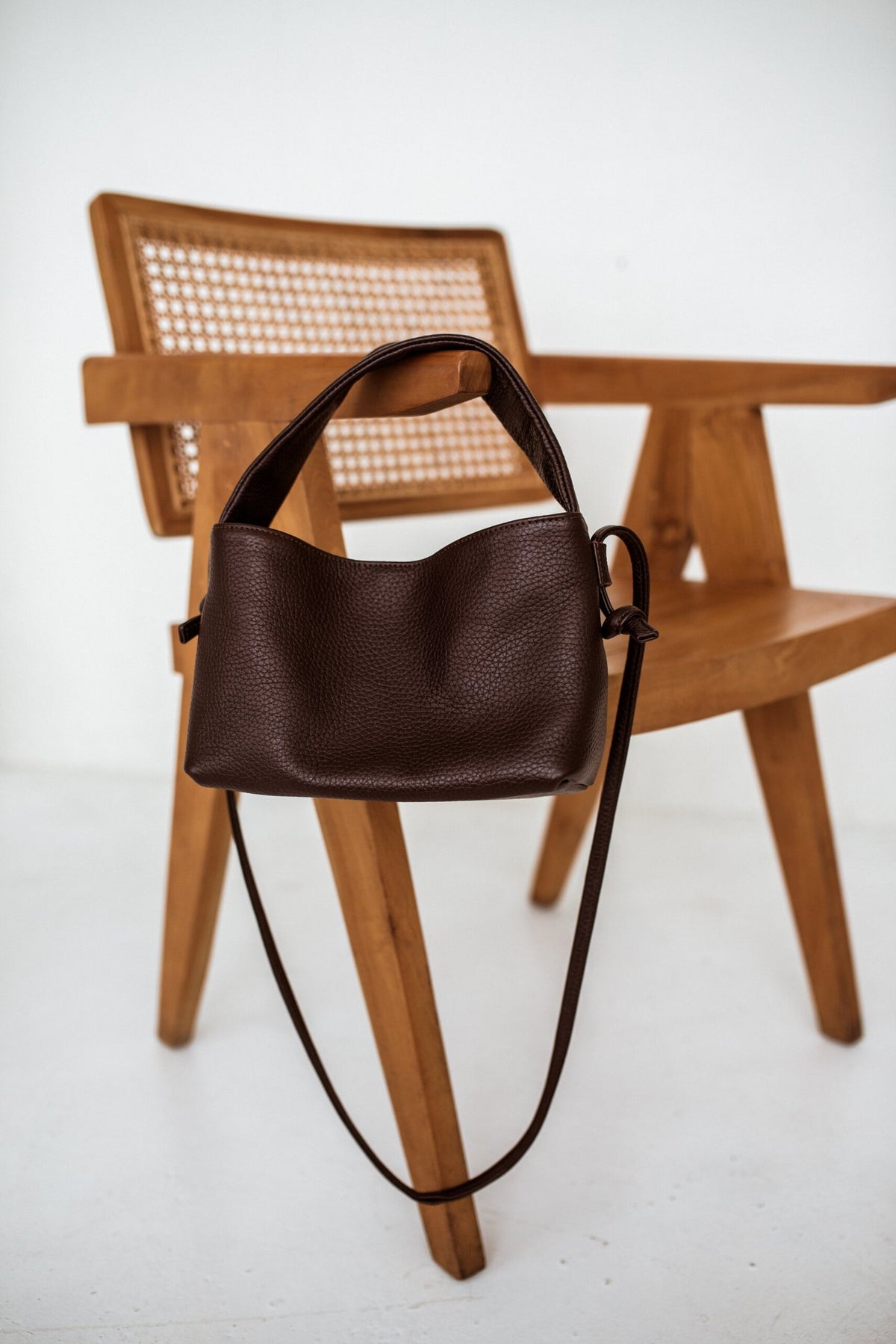 5. Lava flow Crossbody Bag MERU in dark brown leather draped over a wooden chair
