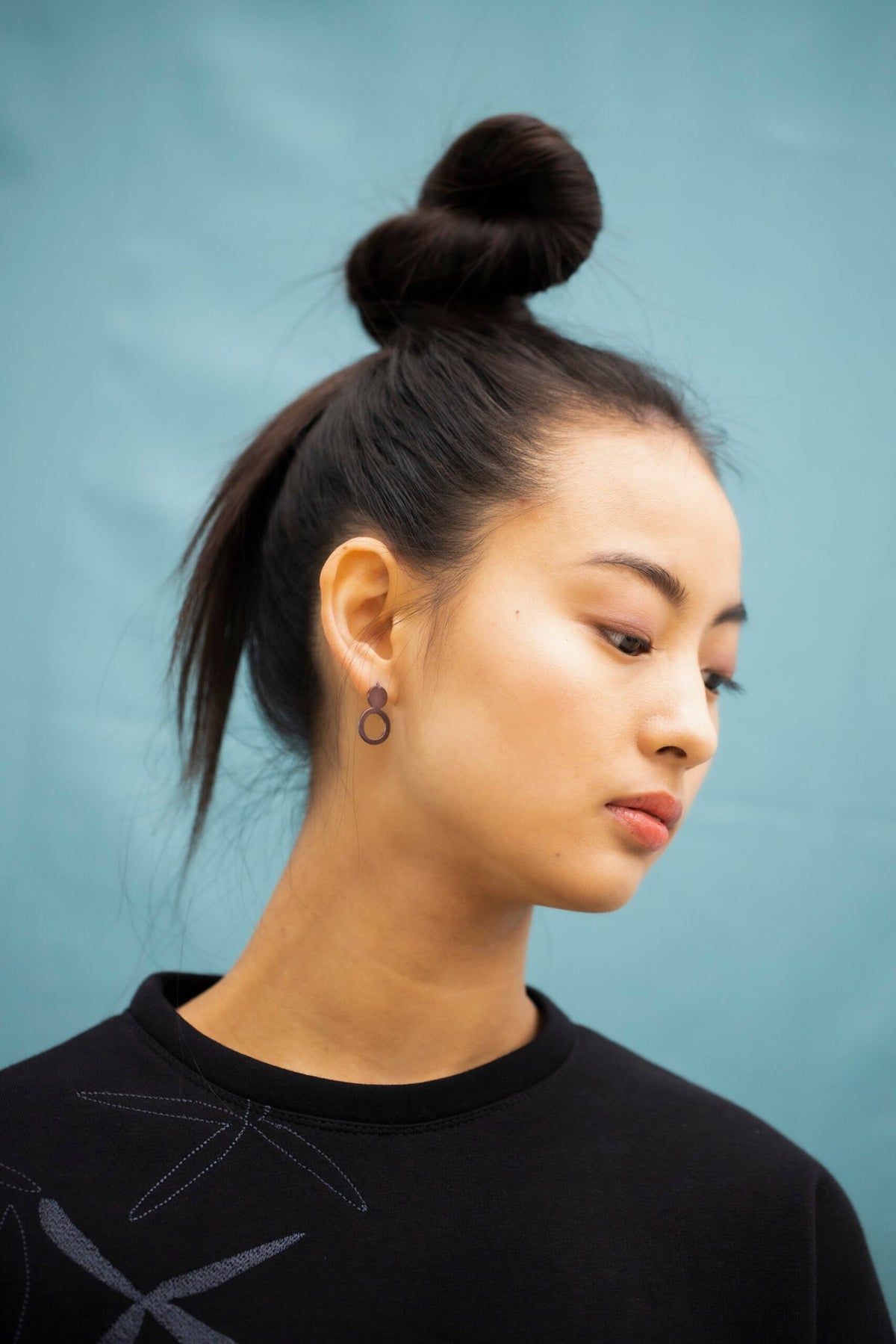6. Woman with Lentsius Arc Purple earrings, styled with a top bun, against a blue background