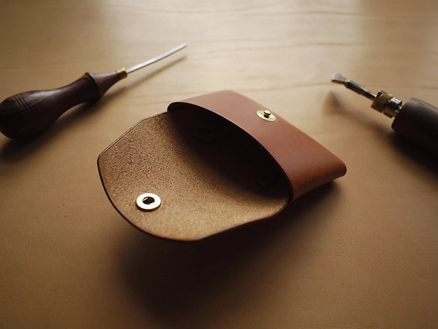 3. Open view of Mirgoods Button Leather Wallet in cognac, highlighting interior space and brass snap button, with leather crafting tools