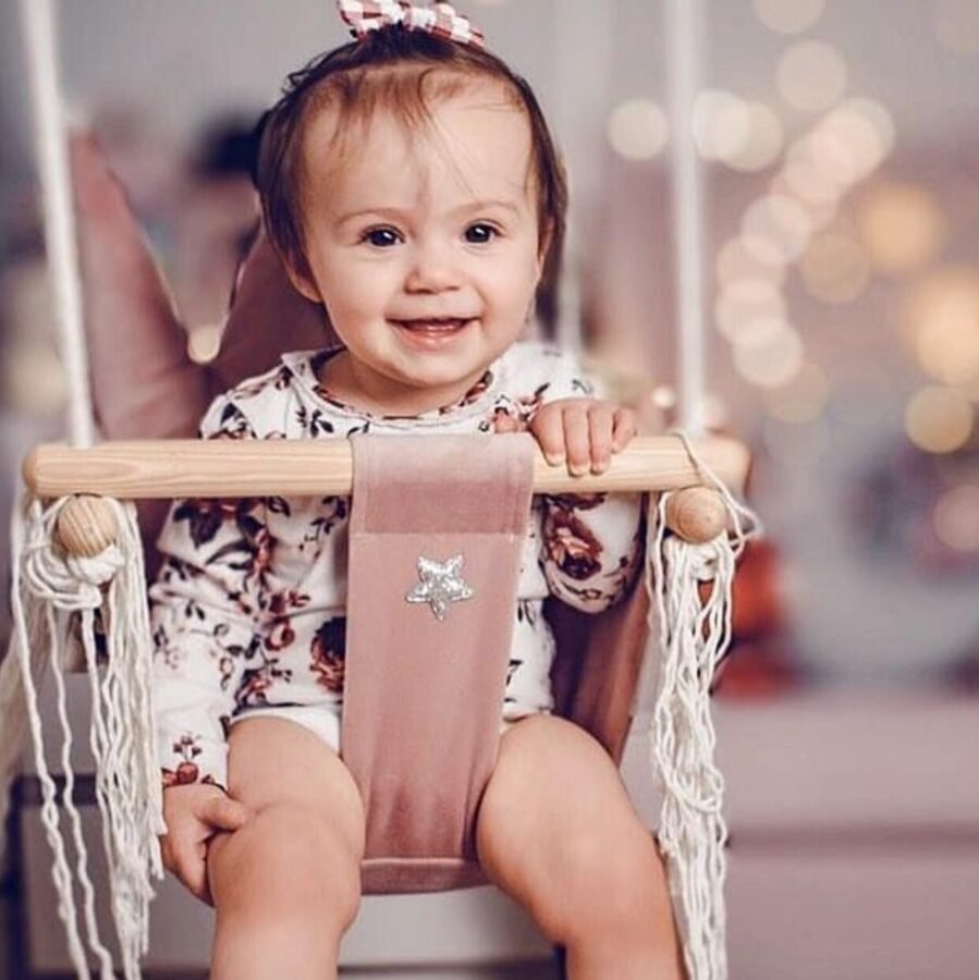 2. Smiling baby in dusty pink crown-shaped swing with floral outfit in softly lit room