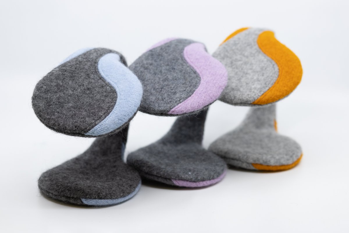 2. Studio shot of HERTTA felted wool earmuffs in medium grey with light blue, purple, and orange accents, displayed in a row