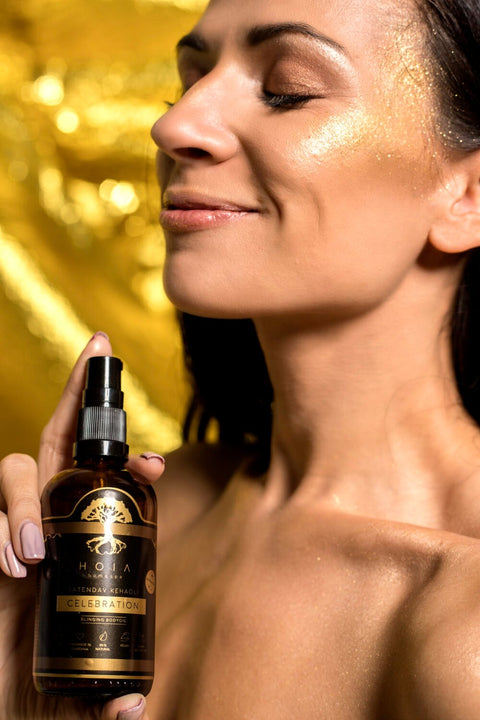 1. Woman holding HOIA homespa Shimmering Body Oil with golden glow on skin, lifestyle setting
