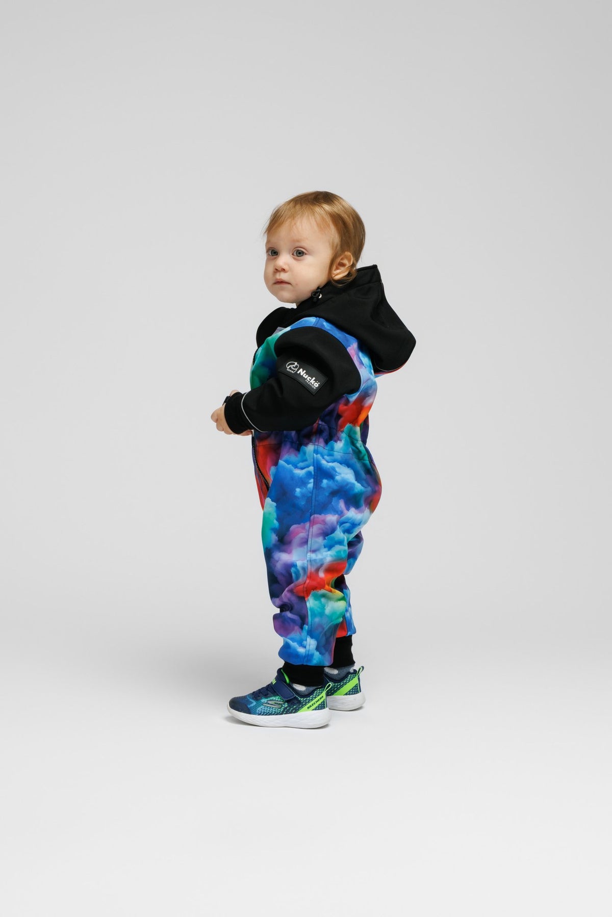 8. Side view of toddler in colorful softshell onesie with black hood, standing on white background