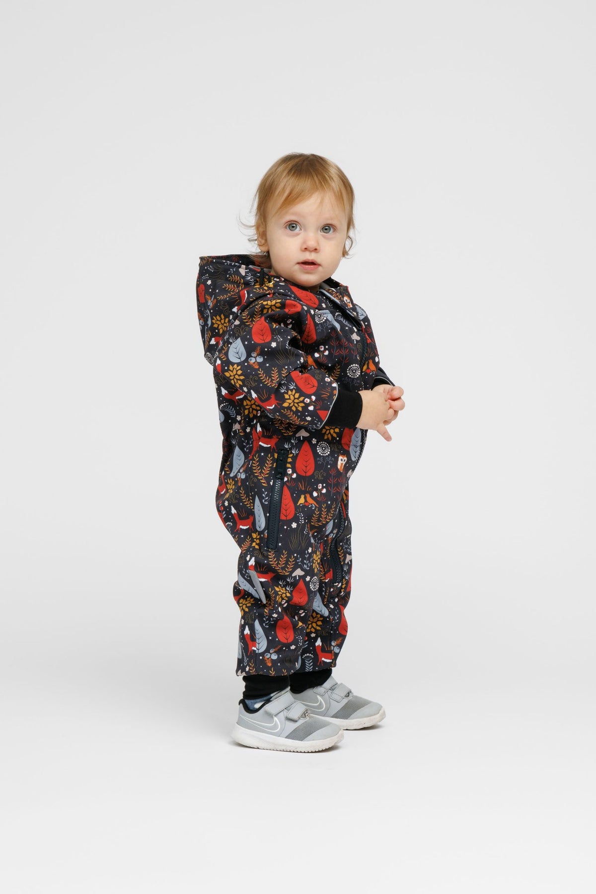 4. Toddler in Nuckö softshell onesie with forest print, standing sideways in studio