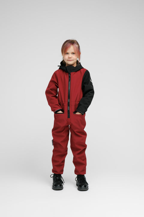 4. Child standing in Nuckö sunset red softshell onesie with black hood and sleeves, showing front view and zippered pockets