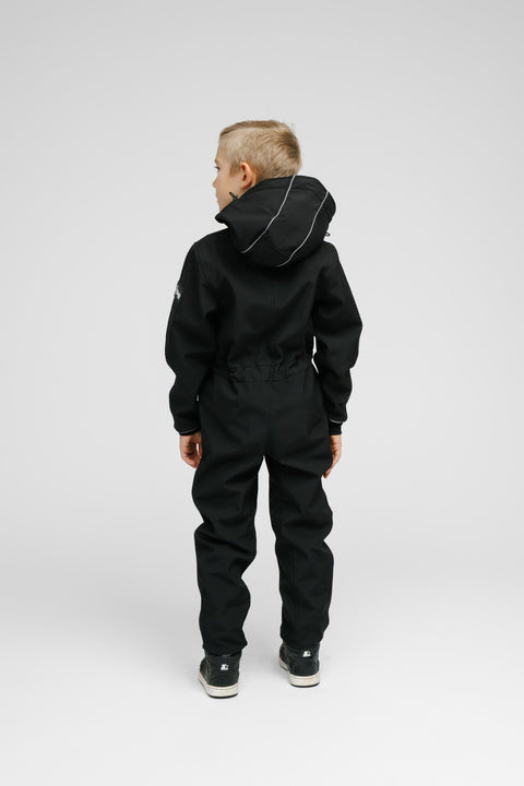 3. Back view of child in black softshell onesie with hood and blue sneakers in studio