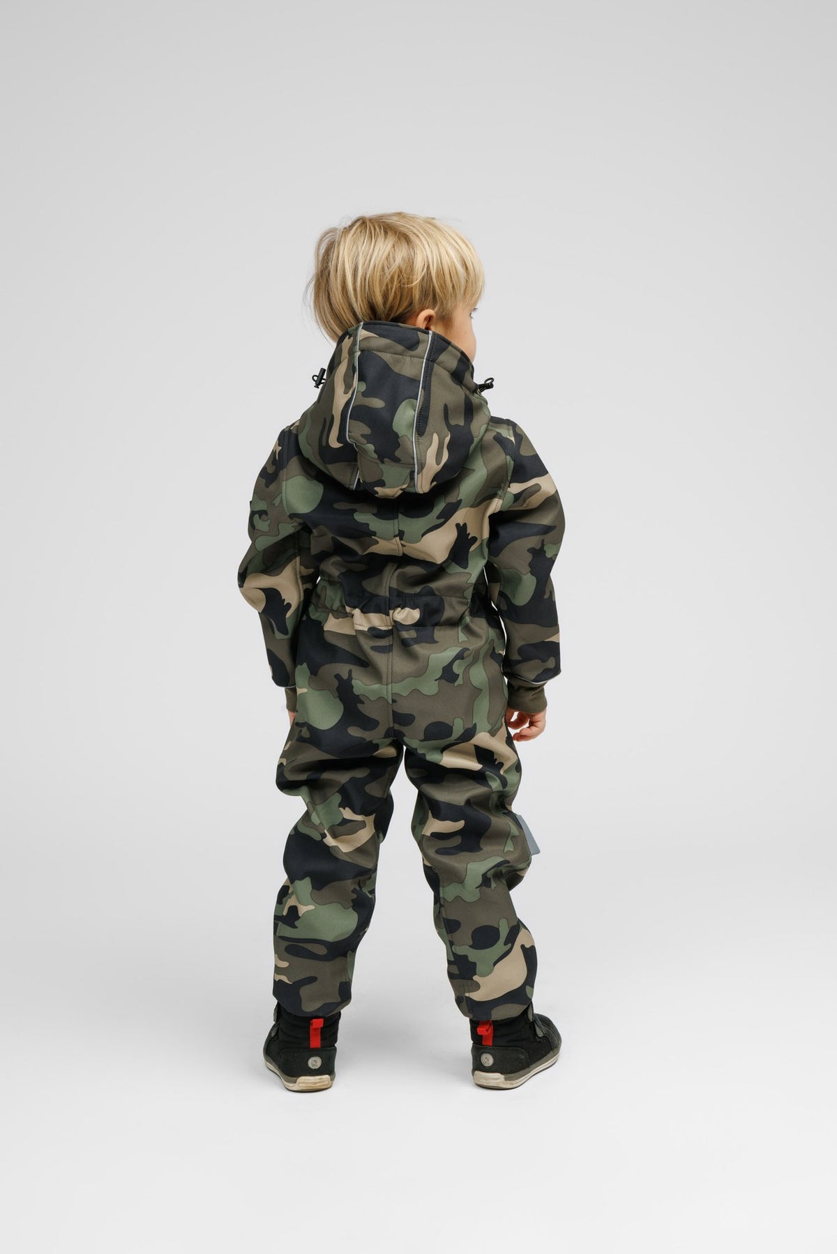 2. Back view of child in Nuckö camouflage softshell onesie, highlighting adjustable waist and hood, reflective stripes visible, studio background
