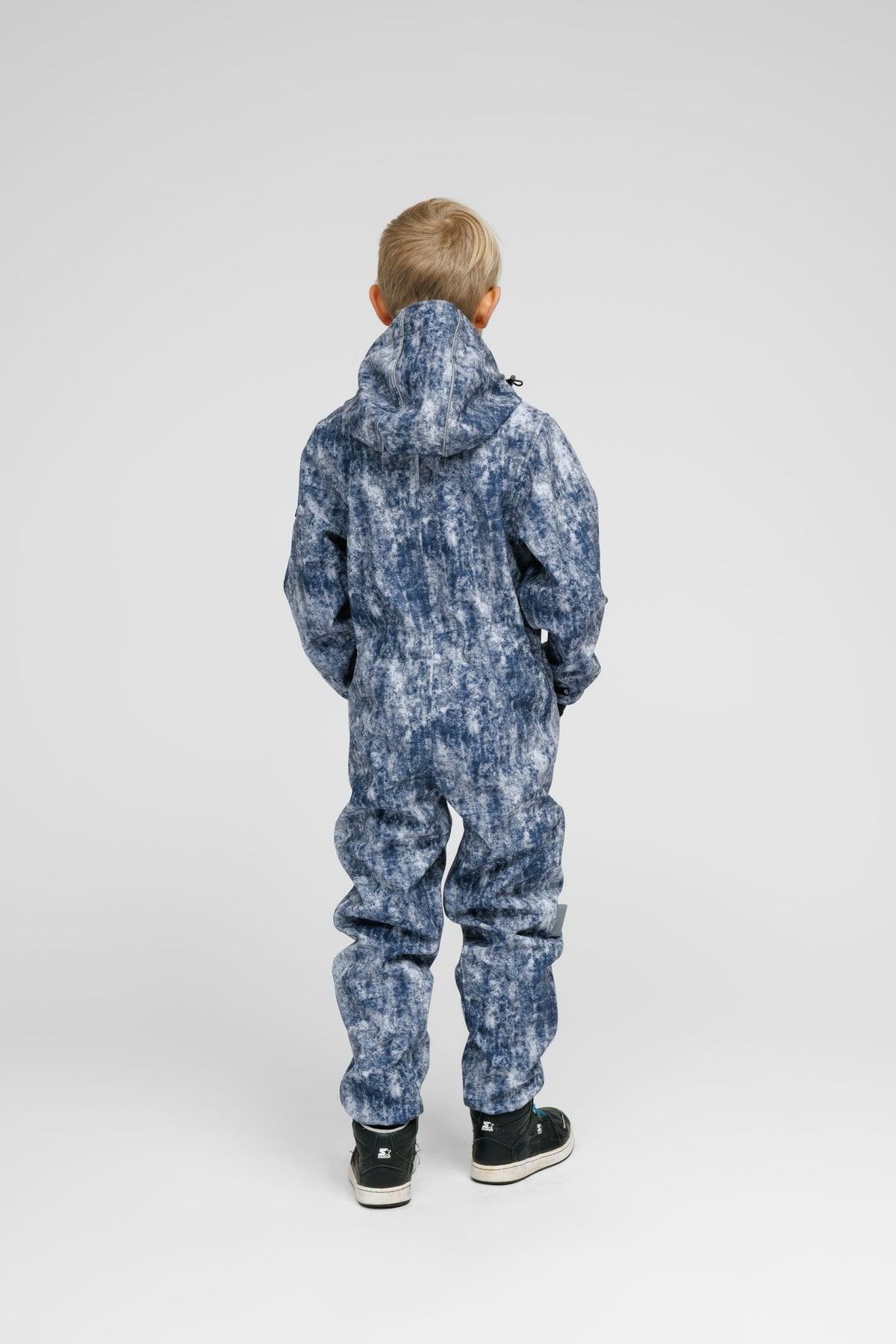 2. Back view of child in blue patterned softshell onesie with hood and black sneakers in studio