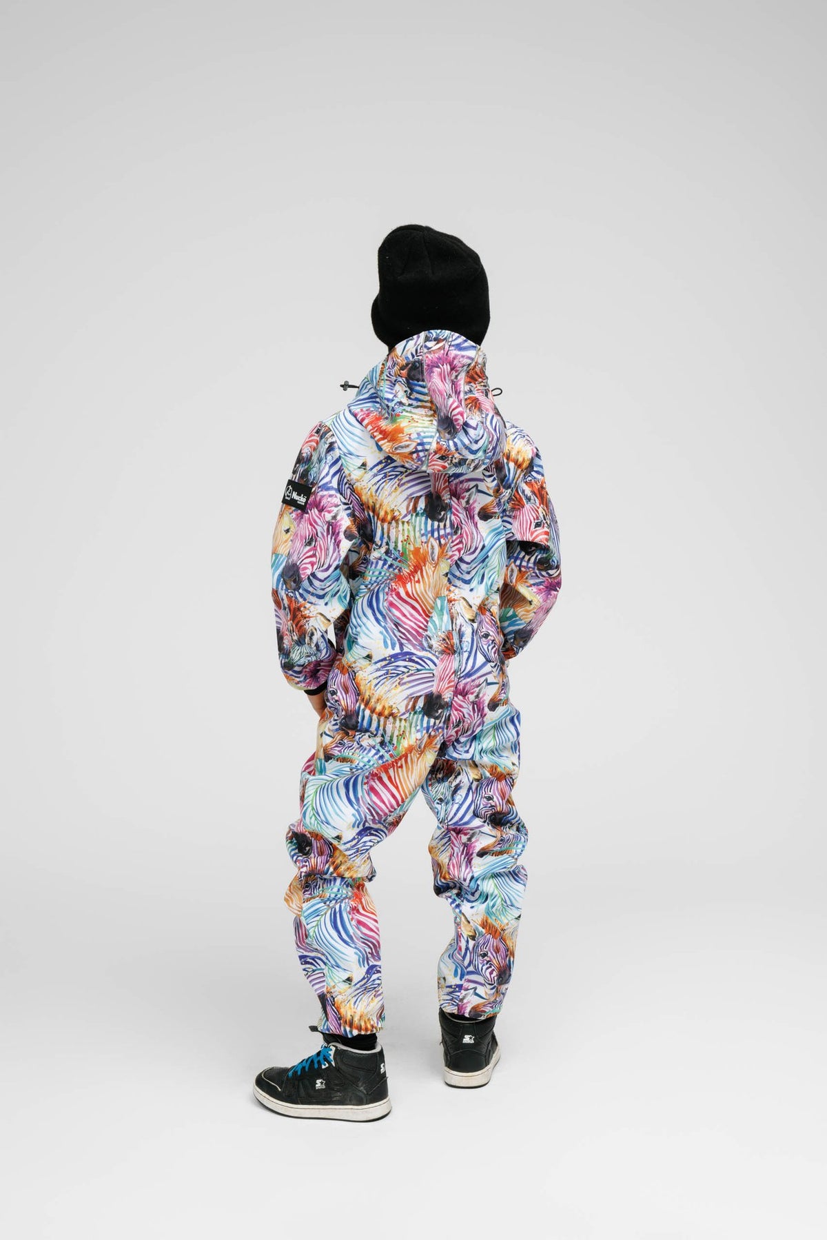 4. Back view of child in Nuckö rainbow softshell onesie with black beanie, studio setting