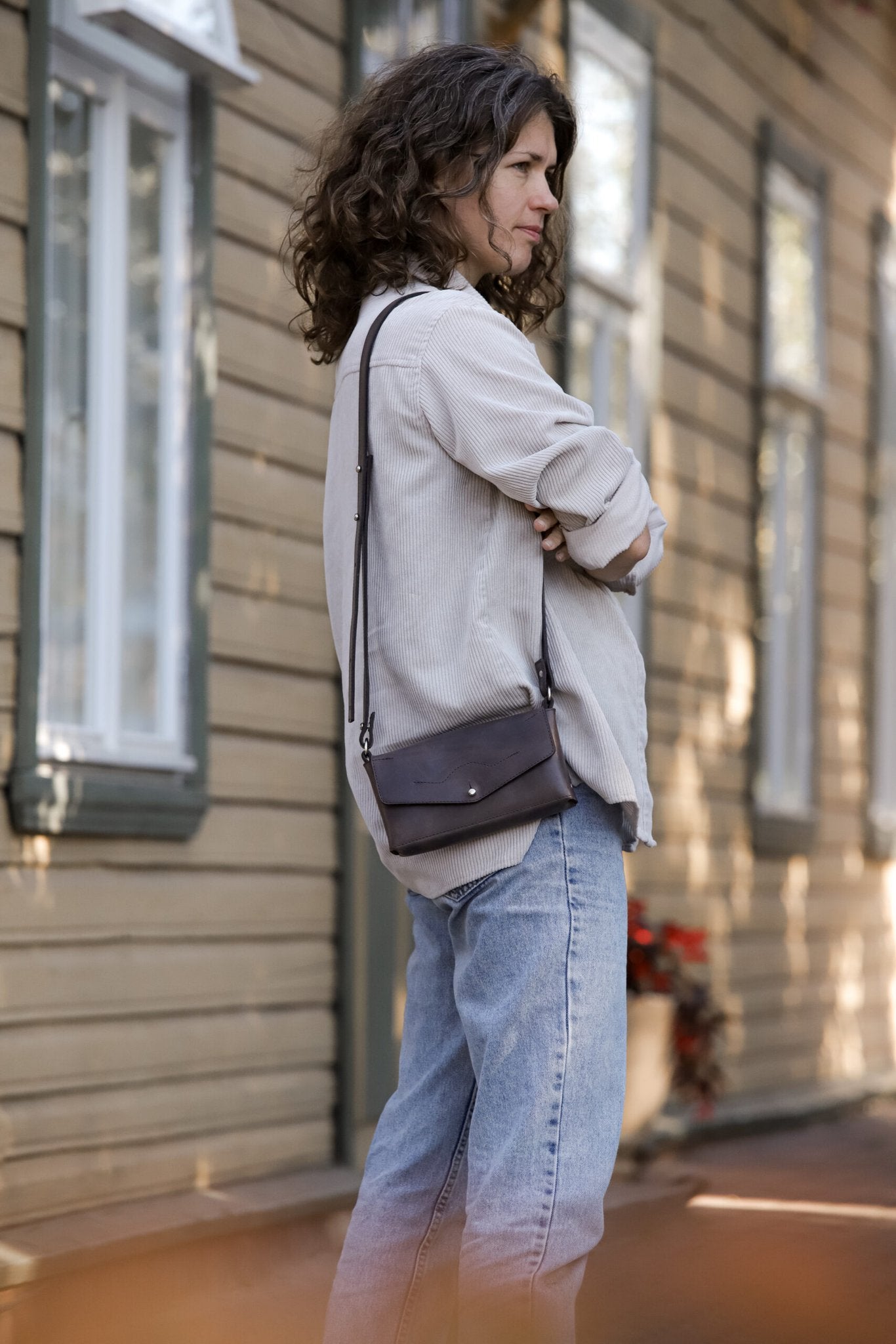 1. Woman wearing KOKUKA crossbody leather bag in brown by eleriinseim, styled casually outdoors