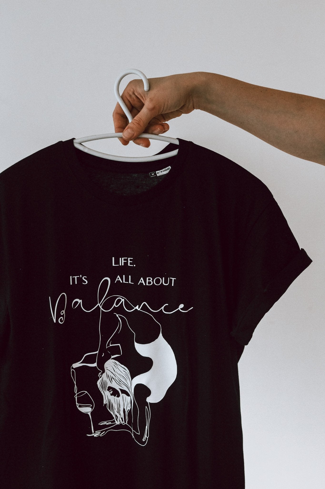 6. Black 'It's All About Balance' T-shirt by Black Giraffe Brand on hanger, showcasing design and rolled-up sleeves