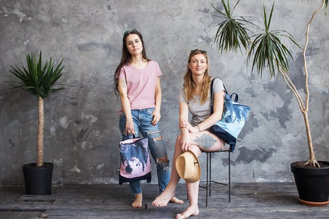 1. Two women showcasing Muni Watercolor backpacks in pink and blue in a lifestyle setting