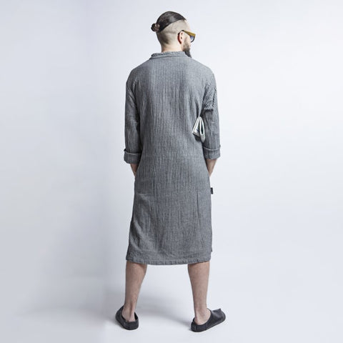 2. Back view of man wearing KOOSdisain black and gray fishbone pattern linen dress, highlighting fabric texture and length