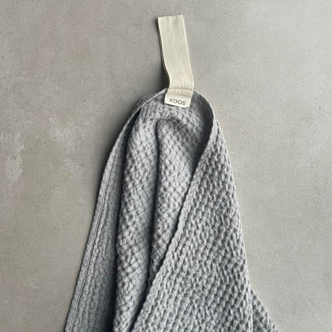 1. Gray waffle fabric towel with white cotton hanger on concrete background, featuring KOOSdisain label