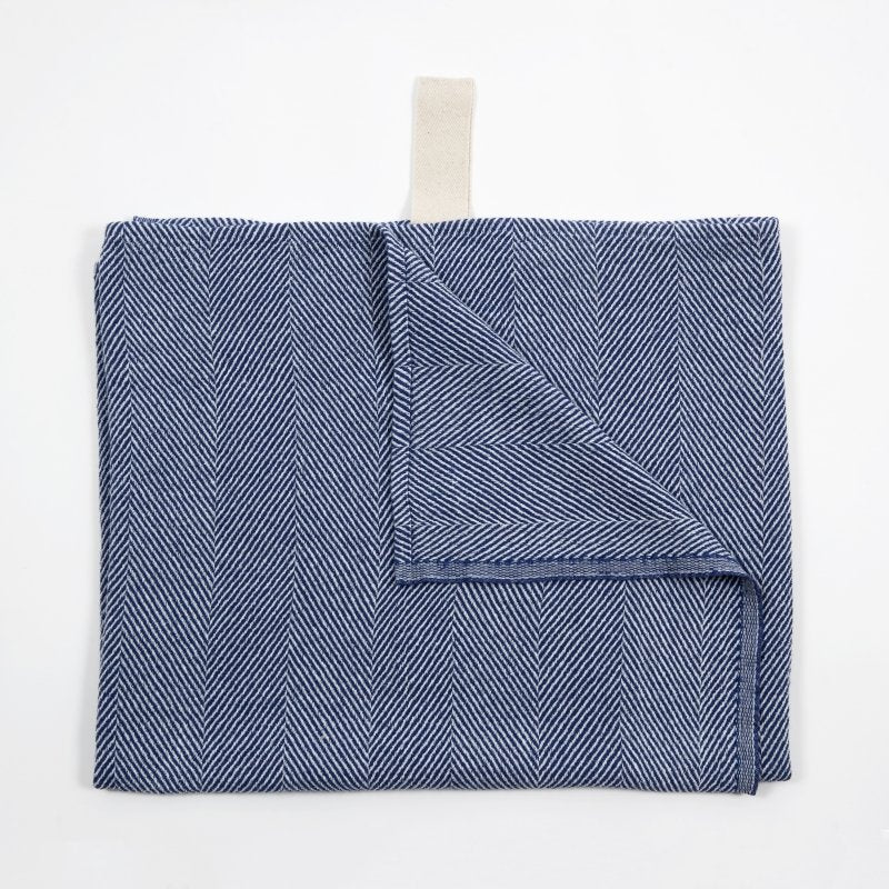 3. Blue linen towel with fishbone pattern partially folded, showing white hanger, on white background