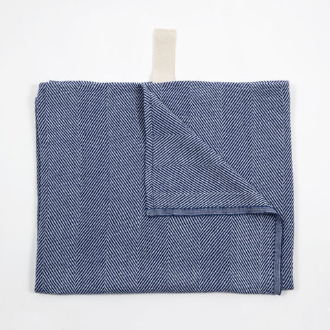 3. Blue linen towel with fishbone pattern partially folded, showing white hanger, on white background