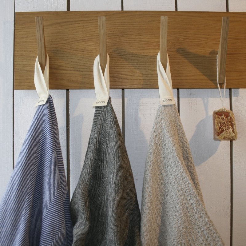 7. Three linen towels in blue, grey, and beige hanging on wooden hooks with KOOS labels