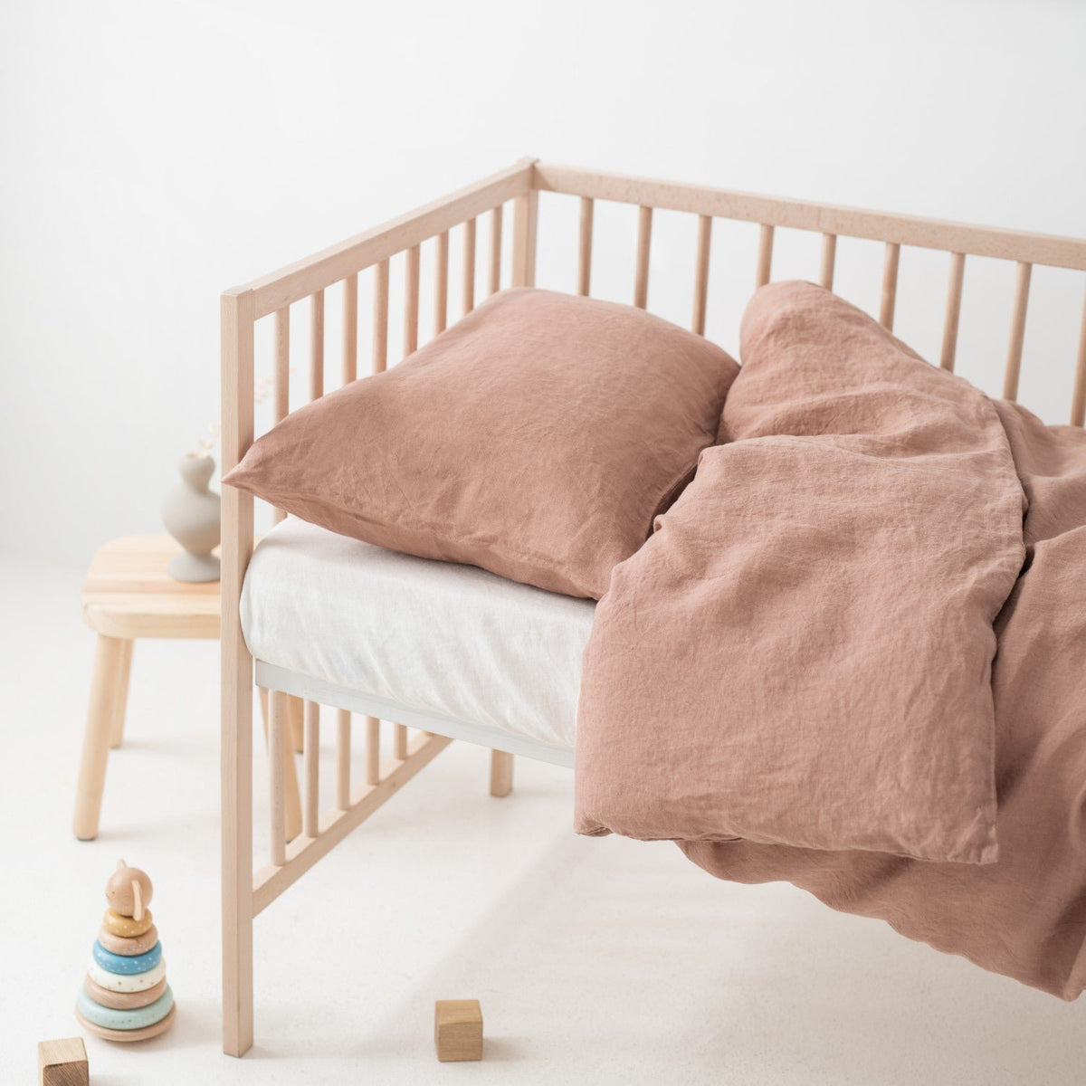 10. Side view of crib with cafe creme linen duvet cover and pillowcase, wooden toys and decor