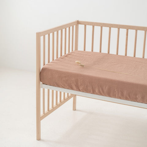 1. Cafe creme linen fitted sheet on a wooden crib in a minimalist room, showcasing the soft texture and elastic hem