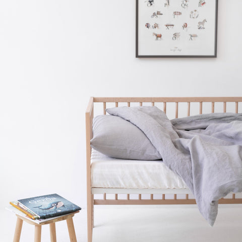 1. Light grey linen duvet cover set on a crib with a book on a stool, in a bright and airy children's room