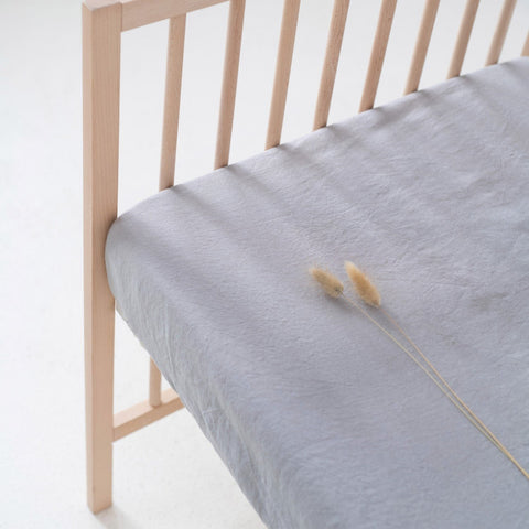 4. Close-up of light grey linen fitted sheet on a crib, showing fabric texture and elastic hem detail