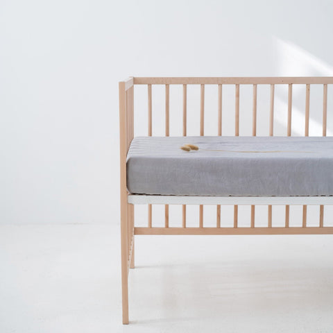 3. Light grey linen fitted sheet on a crib in a bright room, emphasizing the snug fit and soft material