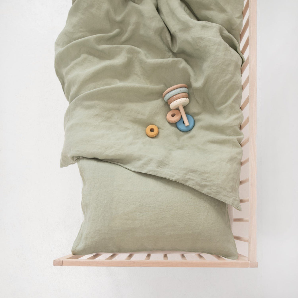 4. Sage green linen duvet cover and pillowcase on a crib with wooden toys