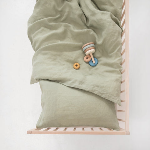 4. Sage green linen duvet cover and pillowcase on a crib with wooden toys