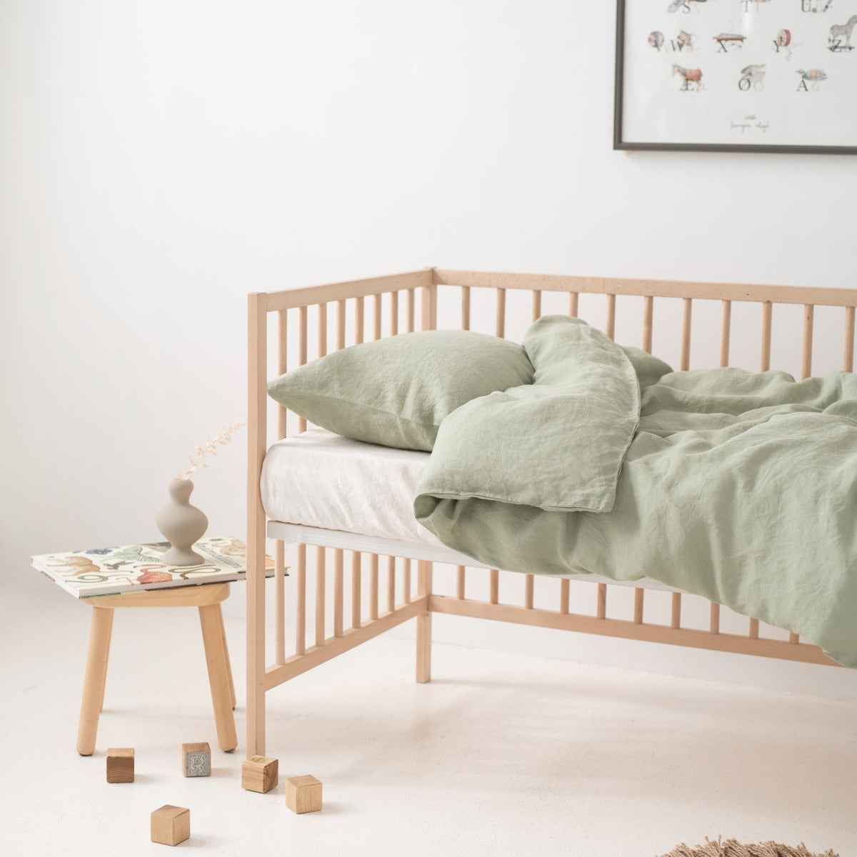 8. Crib with sage green linen duvet cover set, side table, and decor