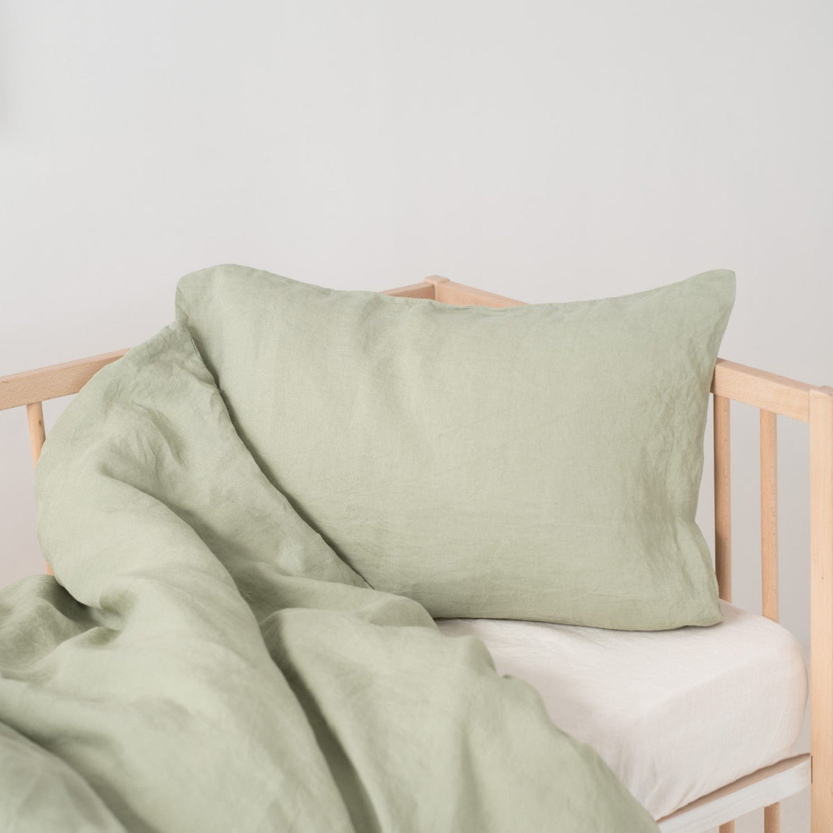 10. Sage green linen duvet cover and pillowcase on crib, showing texture