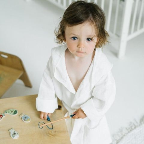 1. Child wearing white linen bathrobe with hood, playing with toys in a bright room